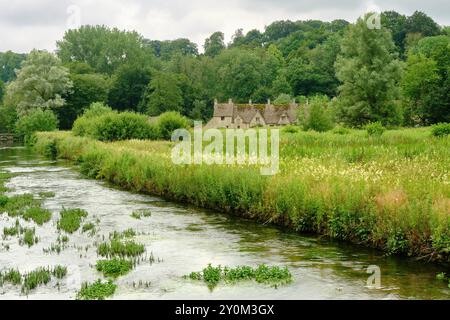 Blick über River Coln und Rack Isle Wasserwiese zu den malerischen Arlington Row Cottages, Bibury, Cotswolds, England, Großbritannien Stockfoto