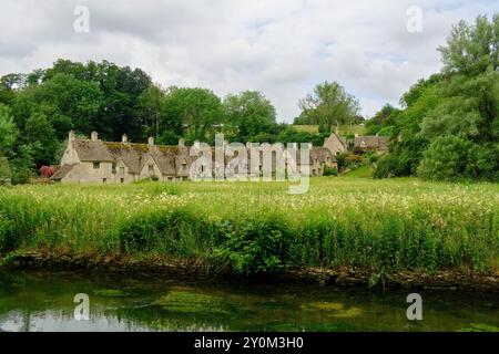 Blick über River Coln und Rack Isle Wasserwiese zu den malerischen Arlington Row Cottages, Bibury, Cotswolds, England, Großbritannien Stockfoto