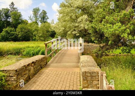 Blick auf eine hölzerne Fußgängerbrücke über den Coln zur Rack Isle Wasserwiese im Cotswold Dorf Bibury, England, Großbritannien Stockfoto