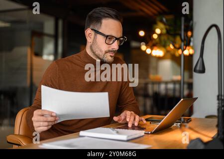 Fokussierter Business Manager in Brillenprüfung Finanzberichte und Verwendung eines Laptops am Schreibtisch im Büro Stockfoto