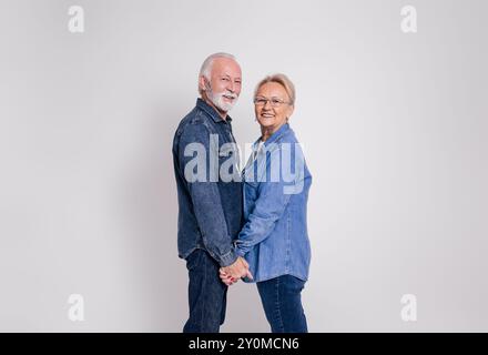 Seitenansicht des liebevollen, reiferen Ehemanns und der Frau, die Hände halten und in die Kamera lächeln auf weißem Hintergrund Stockfoto
