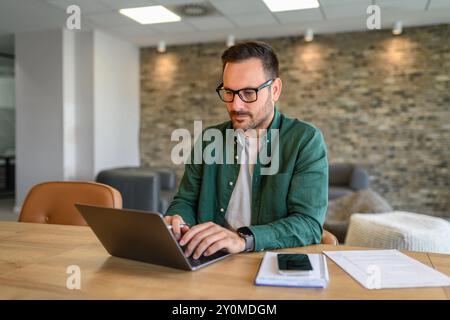 Porträt des Marketing-Managers, der über einen Laptop schreibt, während er ernsthaft am Schreibtisch im Büro arbeitet Stockfoto