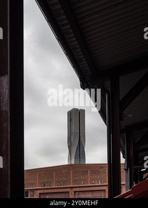 Ein markanter Wolkenkratzer erhebt sich in Göteborg über Industriegebäuden und zeigt moderne Architektur vor einem grauen, bewölkten Himmel. Stockfoto