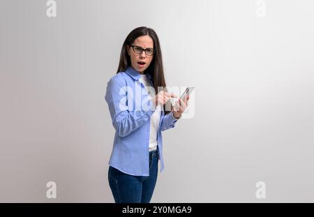 Porträt einer schockierten Geschäftsfrau, die auf das Smartphone zeigt und auf die Kamera auf weißem Hintergrund blickt Stockfoto