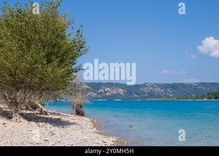 Ein Kieselstrand des Sees Sainte-Croix in Frankreich, mit blauem Wasser unter einem hellen Sommerhimmel, Reiseziel Hintergrund mit Kopierraum Stockfoto