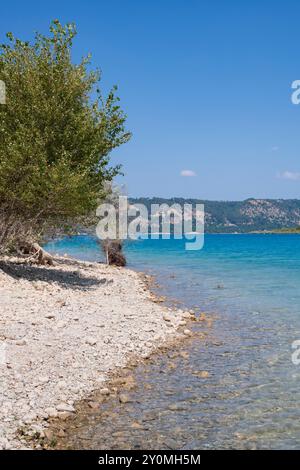 Vertikaler Blick auf den Kiesstrand des Sees Sainte-Croix in Südfrankreich mit blauem Wasser und klarem Sommerhimmel, der eine ruhige Szene schafft Stockfoto