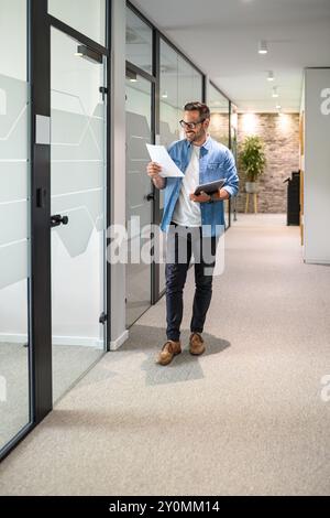 Ein glücklicher Verkäufer hält einen Laptop und prüft den Verkaufsbericht, während er durch den Bürokorridor geht Stockfoto