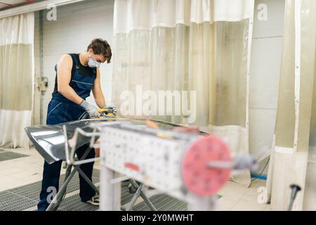 Fernansicht des professionellen Autoservice-männlichen Arbeiters, der schwarze Luxus-Autohaube in der Autoreparaturwerkstatt mit Orbitalpolierer poliert. Stockfoto