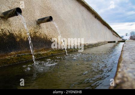 Zeitlupe frisches kaltes Quellwasser fließt in Dorfbrunnen, Wasserrinne für viele Tiere Stockfoto