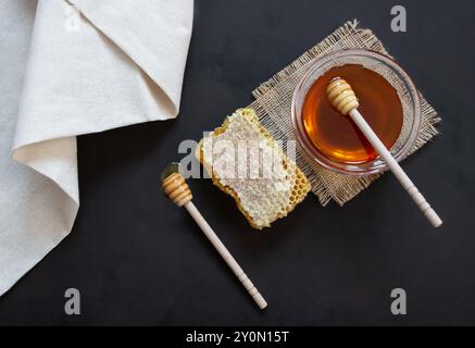 Stück Bienenwabenbiologischer frischer flüssiger Honig in Glasschale mit Pendelarm auf rustikalem Hintergrund, gesundes Essen Stockfoto
