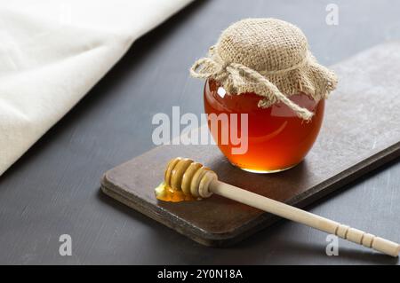 Organischer frischer flüssiger Honig im Glas oder in der Schüssel mit Dipper auf rustikalem Hintergrund, gesundes Essen Stockfoto