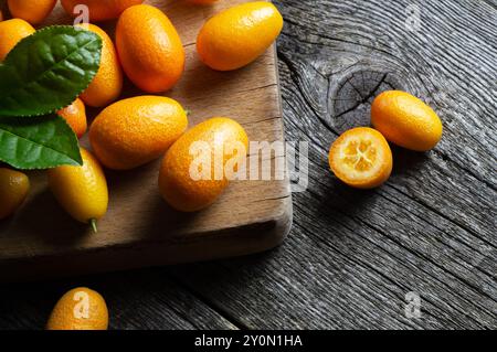 Frische reife Kumquat-Früchte mit Schneidebrett oder Sacksack auf hölzernem Hintergrund, fortunella margarita Stockfoto