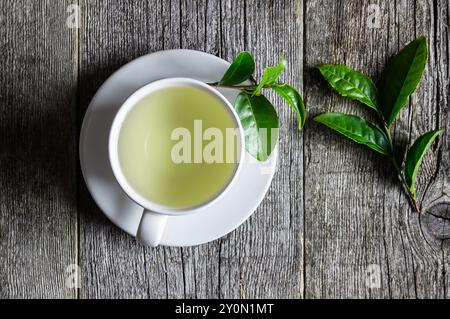 Glas- oder Keramikbecher grüner Tee mit frischen Teeblättern auf rustikalem Tisch, Heißgetränk-Konzept Stockfoto