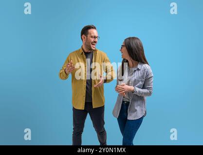 Ekstatischer Geschäftsmann lacht und diskutiert Ideen mit weiblicher Kollegin auf isoliertem blauem Hintergrund Stockfoto