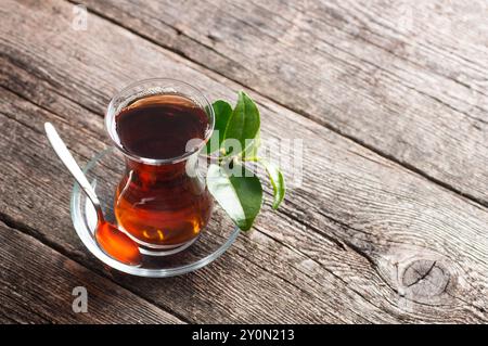 Eine Glasschale schwarzen Tees aus der Teekanne mit frischen Teeblättern, traditionelles türkisches Heißgetränk Stockfoto