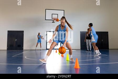 Dribbling Basketball um Kegel, weibliche Basketballspielerin, die im Fitnessstudio trainiert Stockfoto