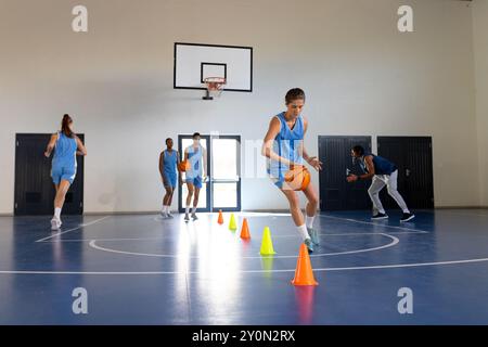 Dribbeln von Basketball um Kegel, weibliches Athletentraining im Schulstudio, Kopierraum Stockfoto