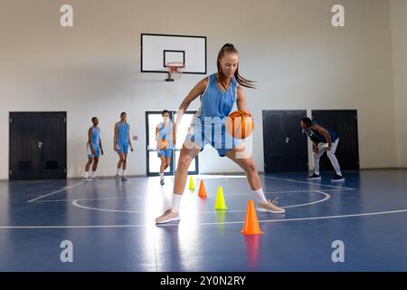 Dribbeln von Basketball um Kegel, weibliches Athletentraining im Indoor Gym Stockfoto