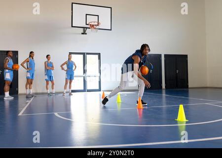 Dribbeln von Basketball um Kegel, Coach Training weiblicher Basketballmannschaft im Fitnessstudio, Kopierraum Stockfoto