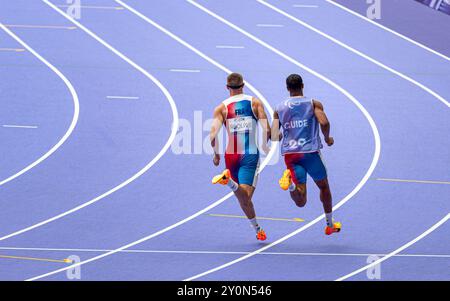 Der blinde französische Paralympic-Athlet Timothée Adolphe mit seinem Reiseleiter lief für die 400-m-Strecke im Stade de France für die Paralympischen Spiele 2024 in Paris. Stockfoto