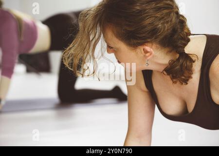 Der Yogalehrer zeigt seine Pose, während die Schüler im Lichtstudio folgen. Gruppenübung am Morgen mit der Frauenklasse mittleren Alters Stockfoto