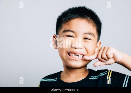 Kind ein asiatischer Junge hebt die Zahnpflege hervor, indem er auf den fehlenden Vorderzahn zeigt. Weißer Hintergrund Stockfoto