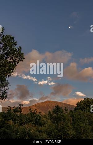 Der fast volle Halbmond erhebt sich über dem Berg Iguaque, in den östlichen Anden Zentral-Kolumbiens, auf einem klaren Himmel bei Sonnenuntergang. Stockfoto