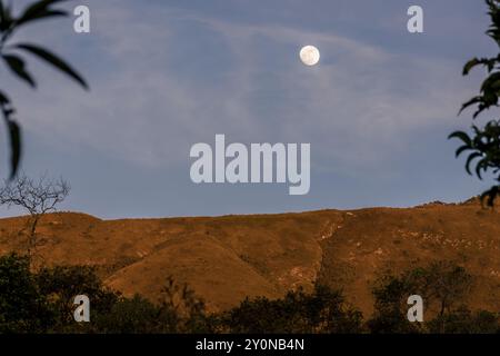 Der fast volle Halbmond erhebt sich über dem Berg Iguaque, in den östlichen Anden Zentral-Kolumbiens, an einem feenklaren Himmel bei Sonnenuntergang. Stockfoto