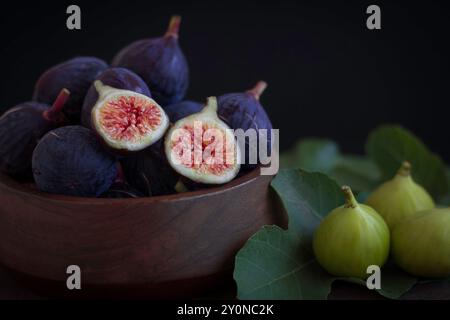 Frisch gepflückte violette und grüne Feigen eine Holzschale mit Feigenblättern Stockfoto