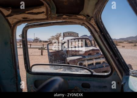 Ein sehr alter, verlassener Lastwagen im Wüstensand von Solitaire, Namibia, durch das Fenster eines anderen verlassenen Lastwagens gesehen Stockfoto