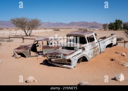 Zwei alte, verlassene Autos, halb in den Wüstensand Namibias gesunken Stockfoto