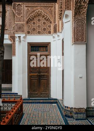 Ein wunderschön gestalteter Flur zeigt kunstvolle architektonische Details und eine Holztür in einem marokkanischen Innenhof mit lebendigen Fliesenmustern. Stockfoto