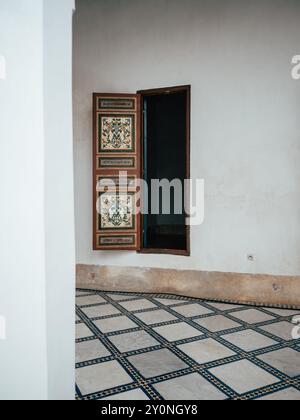 Das Zimmer verfügt über eine wunderschön gearbeitete Holztür mit komplizierten Designs, die offen ist, um Licht hereinzulassen. Der elegante Fliesenboden trägt zur Tra bei Stockfoto