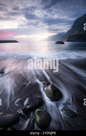 Schwarzer Sandstrand von Seixal, Dorf auf der Nordseite der Insel Madeira, Portugal, mit wunderschönen Kieselsteinen im Vordergrund, lange Exposition, Sonneneinstrahlung Stockfoto