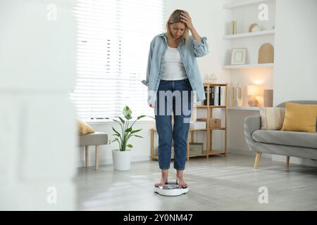 Wechseljahre, Gewichtszunahme. Besorgte Frau, die zu Hause auf der Waage steht Stockfoto