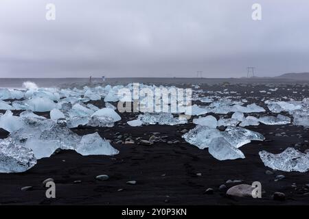 Diamond Beach in Island – transparente Eisberge, die an Land gewaschen werden, auf schwarzem Sandstrand mit Meereslandschaft im Hintergrund. Stockfoto