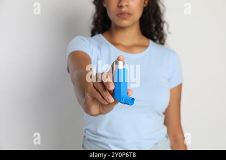 Frau mit Asthma-Inhalator auf hellgrauem Hintergrund, Nahaufnahme Stockfoto