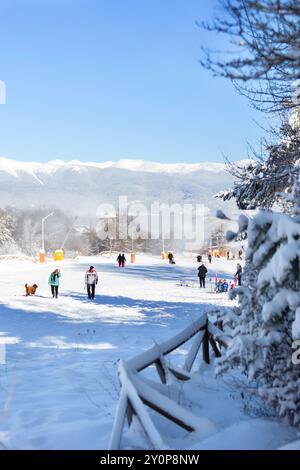 Bansko, Bulgarien - 20. Dezember 2023: Bulgarisches Winterskigebiet Panorama mit Berggipfeln und Skifahrern nahe der Unterstation Stockfoto