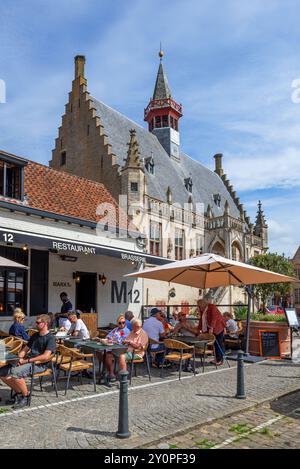 Touristen im Straßencafé der Brasserie Markt 12 / M12 auf dem Marktplatz neben dem Rathaus in der Stadt Damme im Sommer, Westflandern, Belgien Stockfoto