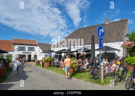 Touristen im Straßencafé des Pubs den Ouden Toren auf dem Marktplatz im Dorf Lissewege bei Brügge im Sommer, Westflandern, Belgien Stockfoto