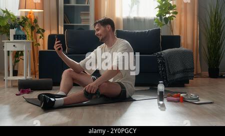 Glücklicher positiver kaukasischer männlicher Mann Mann, der ein Mobiltelefon benutzt, das online telefoniert, nach hartem Sport-Workout mit Daumen nach oben hält Stockfoto