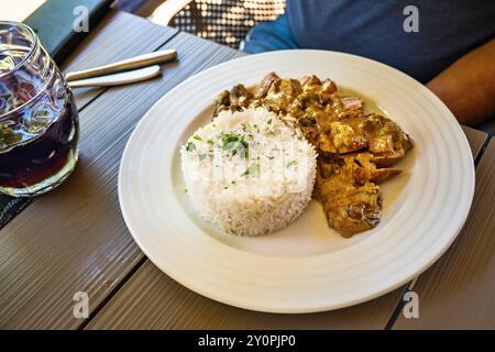 Schweinestück mit Pilzen auf cremiger Sauce, gedünsteter Reis auf weißem Teller auf Restauranttisch. Stockfoto