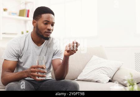 Ein ernster Mann, der bereit ist, eine Pille auf der Couch zu nehmen Stockfoto