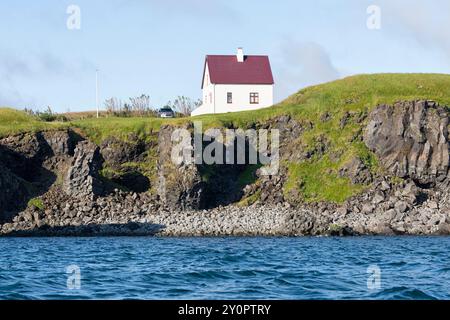Küste mit Vogelklippe und einem weißen Haus vom Wasser aus gesehen. Arnastapi, Snæfellsbær, Halbinsel Snæfellsnes, Westisland Stockfoto