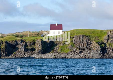 Küste mit Vogelklippe und einem weißen Haus vom Wasser aus gesehen. Arnastapi, Snæfellsbær, Halbinsel Snæfellsnes, Westisland Stockfoto