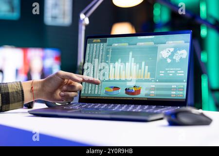 Nahaufnahme einer Person, die auf den Bildschirm zeigt, in dem Finanzdiagramme und -Zahlen angezeigt werden, die den Aktienhandel darstellen. Digitales Notebook auf einem Schreibtisch mit Forex-Trendwerten und Diagrammen. Stockfoto