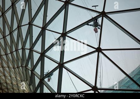 Fensterreiniger arbeiten an der Außenseite eines modernen geometrischen Glasdachs. Stockfoto