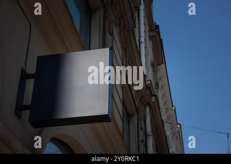 Leere blaue graue quadratische Ladenschilder, die an einer Gebäudefassade hängen und in einer europäischen Stadtstraße vor klarem Himmel sichtbar sind, ideal für Einzelhandelsgeschäfte A Stockfoto