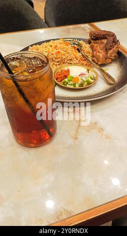 Porträt von Kebuli-Reis (Nasi Kebuli) und Eistee, typisch arabisches Essen, hergestellt in Indonesien auf einem Tisch mit leerem Platz daneben in einem 45-Grad-Winkel Stockfoto