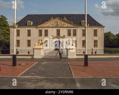 Mann vor einem großen historischen Herrenhaus mit Löwenstatuen und Fahnenmasten bei Tageslicht, dornum, ostfriesland, deutschland Stockfoto